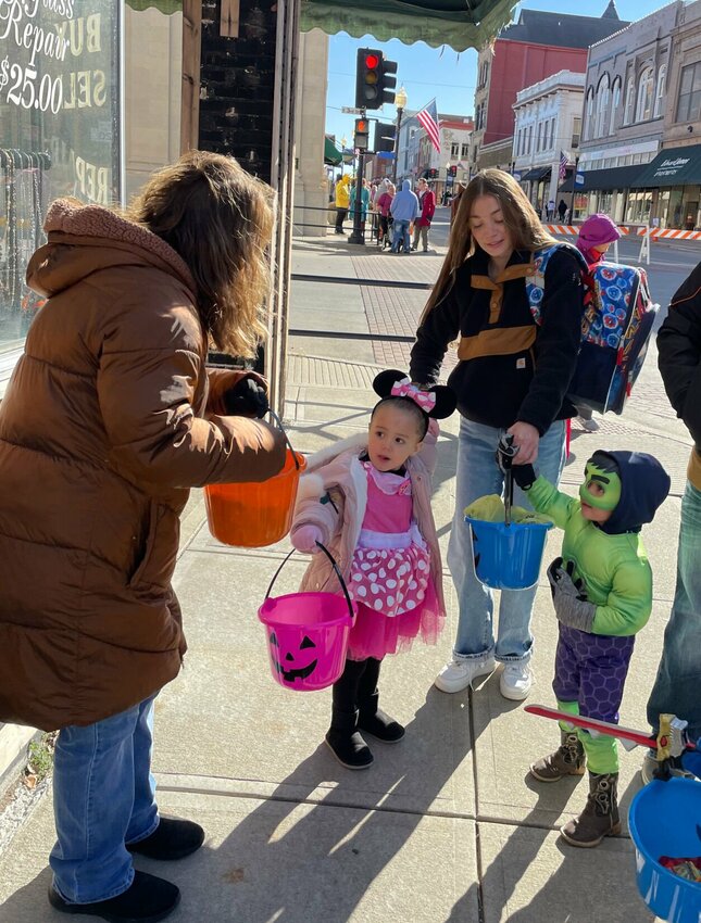 Tracey Gengler with Classic Jewelry hands out candy to Hallie Freitas and Luke Klein on Halloween, Tuesday, Oct. 31 as part of the Downtown Trick or Treat event hosted by Sedalia Main Streets. Gengler was fortunate on a chilly afternoon to be in the warm sunshine.   Photo by Chris Howell | Democrat