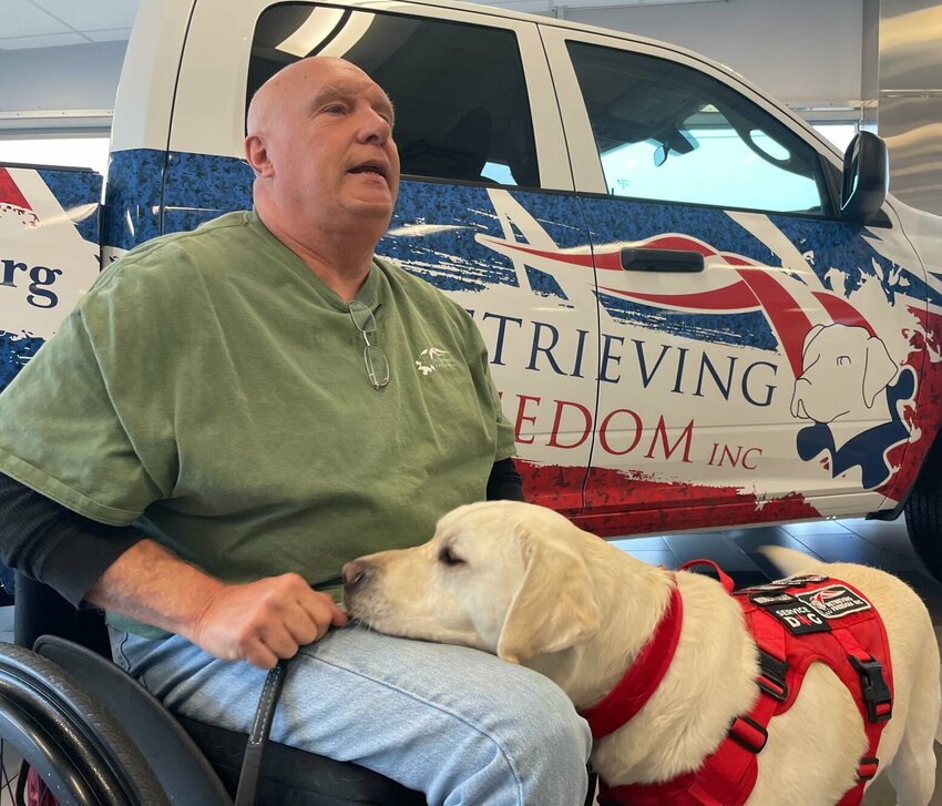 Disabled veteran Michael Wasson and his mobility dog, Dusty, are seen at the W-K Chrysler Dodge Jeep Ram dealership Friday, Dec. 1. The Weymuth family donated new trucks to Retrieving Freedom, a local nonprofit that trains service dogs.   Photo by Chris Howell | Democrat