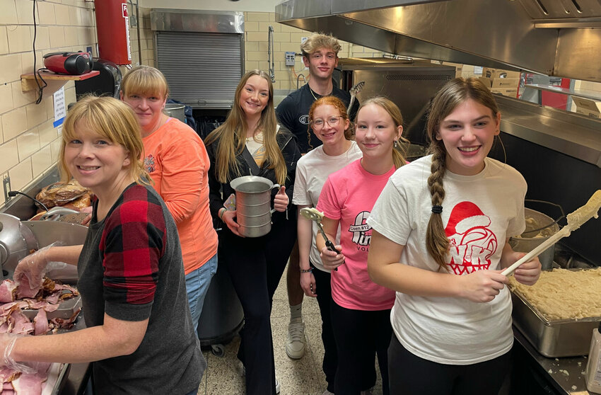 Sacred Heart teacher Jill Bentch slices ham as kitchen helpers Julie Vogel, Emily Jackson, Jared Owens, Cassidy Bentch, Ebrinn Cahill and Bailee Vogel help prepare hundreds of Christmas Eve meals in the Sacred Heart cafeteria kitchen Thursday, Dec. 21.   Photo by Chris Howell | Democrat