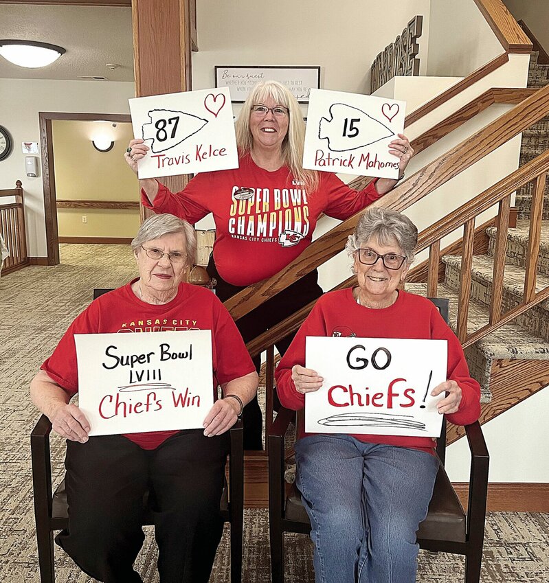 On Wednesday, Jan. 24 at Primrose Retirement Community of Sedalia, Activities Director Connie Chevalier and residents, from left, LaVerne Monsees and Lois King hold signs supporting the Kansas City Chiefs playoff games. This week, a video featuring some of the residents in a Chiefs-related dance routine went viral on social media.   Photo by Faith Bemiss-McKinney | Democrat