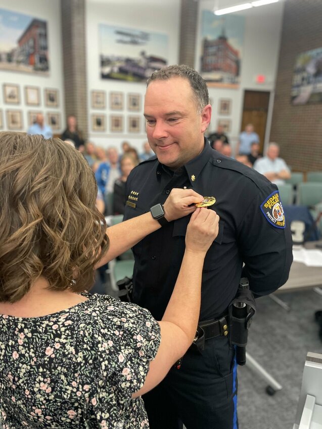 Amy Woolery pins the Chief of Police badge in her husband, David Woolery, during the Sedalia City Council meeting Monday, April 1. Woolery was picked as top cop after a stint as interim chief that began when Matt Wirt took a job as Assistant City Administrator.   Photo by Chris Howell | Democrat