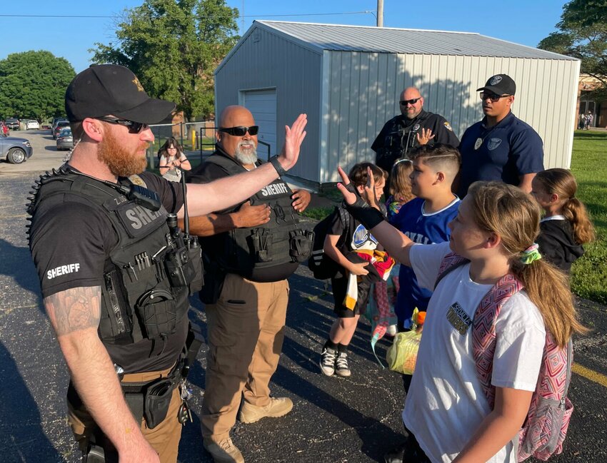 Pettis County Deputy Zack Long high-fives Parkview Elementary student Madison Brandcamp on her final day of school Friday morning, May 17. Seen in the background from left, Pettis County Deputy Larry Parham and Officer John Hammond and Sgt. Daniel Benner of the Sedalia Police Department also greeted the students Friday morning.   Photo by Chris Howell | Democrat