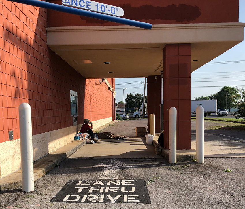 (06/18/22) A couple lived under the drive-thru window at the former Rite Aid drug store on Madison Street for several days. The man takes a drink of water while his wife sleeps under a blanket. She described herself as a former Tyson Foods employee about to be rehired, and said once she&rsquo;s back to work they&rsquo;ll be able to afford housing. The couple asked not to be identified.