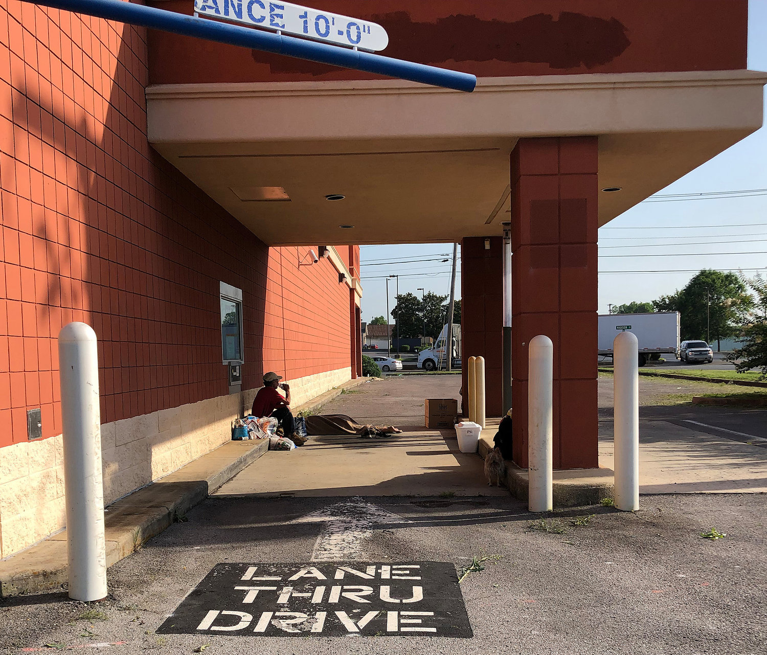 (06/18/22) A couple lived under the drive-thru window at the former Rite Aid drug store on Madison Street for several days. The man takes a drink of water while his wife sleeps under a blanket. She described herself as a former Tyson Foods employee about to be rehired, and said once she’s back to work they’ll be able to afford housing. The couple asked not to be identified.