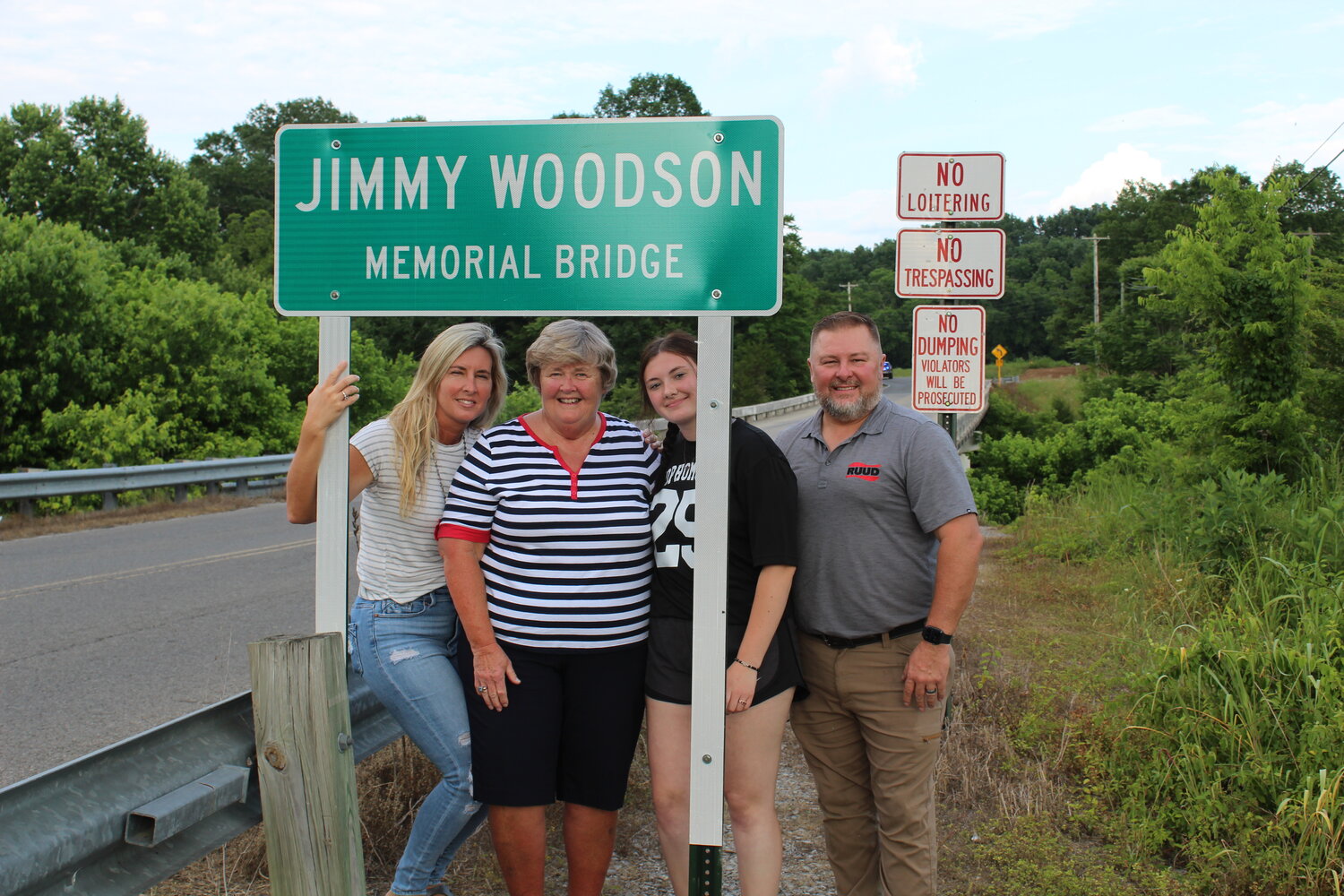 Photo of Woodson family members with sign after the unveiling, from left: Woodson’s daughter Melody Redd, his widow Charlene Woodson, granddaughter Katie Daugherty and son-in-law Jamie Redd.