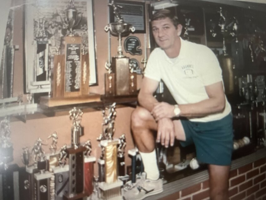 Coach Buddy Hepfer in front of the trophy display case at Arundel High School where he built the successful football and wrestling programs.