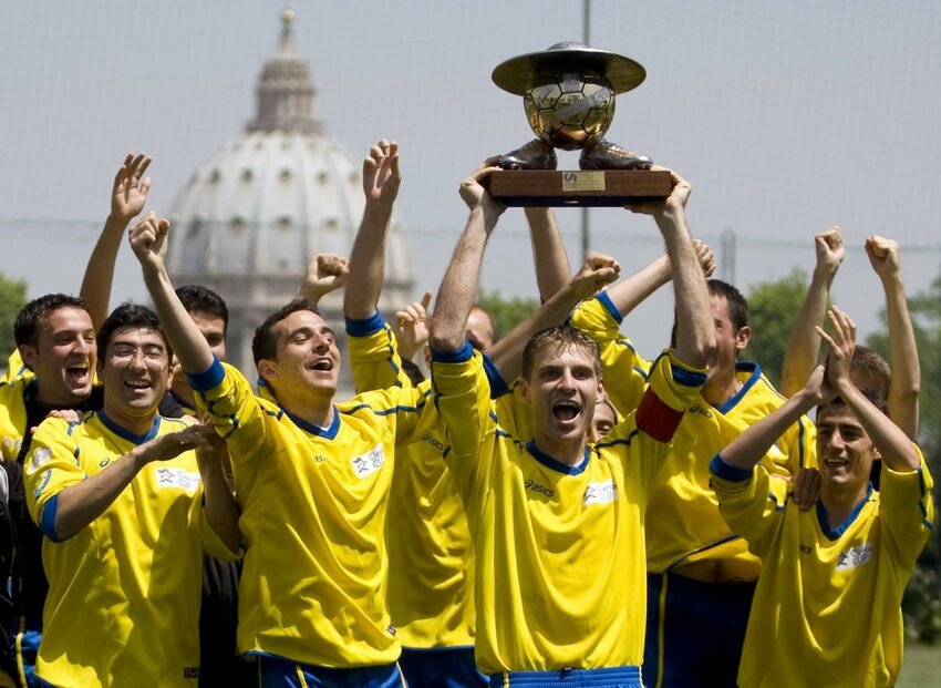 Vatican seminarians hoisting the Clericus Cup trophy, a soccer ball sandwiched between a Cappello Romano (a hat worn by priests) and a pair of cleats.