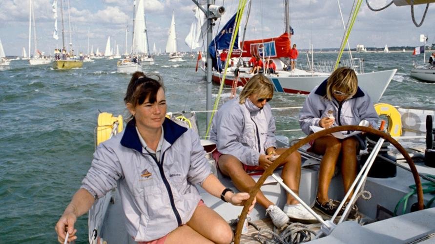 Tracy Edwards at the helm of the 'Maiden' with two of her crew members behind. In 1989, she made history by becoming the first woman to skipper an all-female team at the Whitbread Round the World Race, earning her the Yachtsman of the Year Trophy.