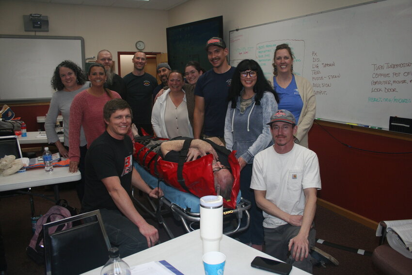 EMT student Scott Lamb is encased in a whole-body vacuum splint to help stabilize a simulated midshaft femur fracture immobilized with a traction splint. Onlookers include the remainder of the EMT students and assistant lab instructors Amy Wetherill and Charles Miller. 