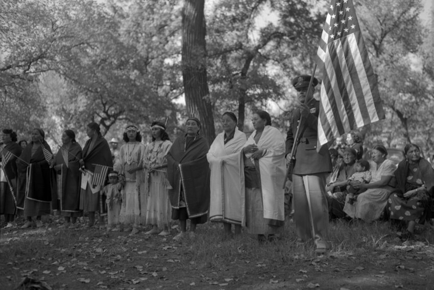 Honor dance welcoming home Pascal Cleatus Poolaw Sr. (far right, holding the flag) after his service in the Korean War. To his right are members of the Kiowa War Mothers. Carnegie, Oklahoma. Poolaw (Kiowa, 1922 to 1967) was considered the most decorated American Indian soldier in history, earning 42 medals and two citations during three wars: World War II, Korean War and Viet Nam. First Sgt. Poolaw was killed carrying a wounded soldier to safety. Photo part of Why We Serve exhibit, which can be previewed at www.historycolorado.org/exhibit/why-we-serve. 