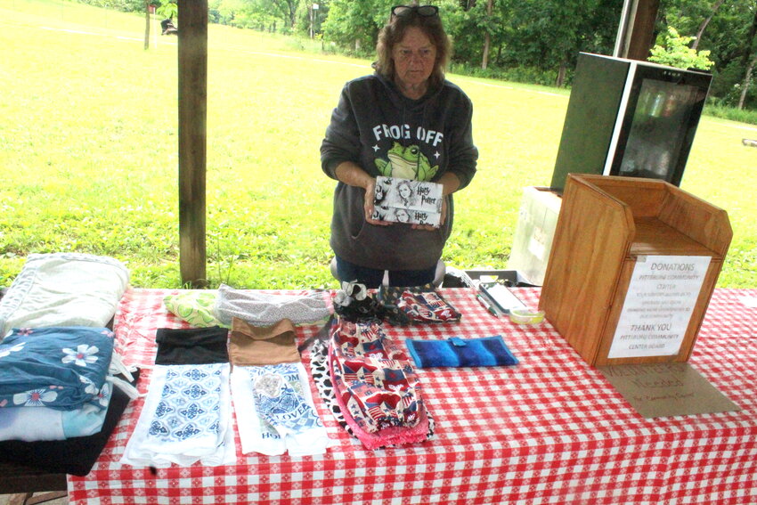 Ellen Berringer, a member of the Pittsburg Community Building Board, showcases some of her  handmade items that were on sale during this past weekend’s Pittsburg Garage Sales. She is holding a Harry Potter themed billfold she created herself, while several of her bags, towels, quilts, and other items are on display nearby. The Pittsburg Community Building Board held garage sales the morning of Saturday, June 7, with a lighter than expected turnout due to the constant rainfall.