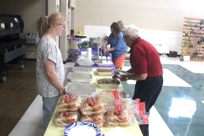 On the left, Liberty Hammer assists Billy Pearson with gathering up his plate Saturday, June 7, during the Hermitage R-IV Alumni Banquet. With being the oldest attending graduate from Hermitage High School, Pearson was given the honor of eating first. The pulled pork and pulled chicken meal was catered by Hickory Pit BBQ. On the right, guests take a moment to look over the collection of Hermitage High School yearbooks on display in the gymnasium.