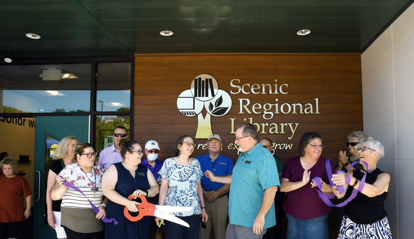 Hermann Area Chamber of Commerce President Gary Watts congratulates Scenic Regional Library trustee Kathi Ham (center, of Hermann) after the ceremonial ribbon cutting Saturday during grand-opening festivities of the Hermann branch. Also pictured (from left) are Karen Holtmeyer, (library trustee), Makayla Baker (branch employee), Steven Campbell (Scenic Regional&rsquo;s executive director), Kasey Wright (manager of the Hermann and New Haven library facilities), John Barry (trustee), Larry Miskel (Gasconade County presiding commissioner), Dan McKinney (executive director of Hermann Area District Hospital), Carla Robertson (trustee), Linda Andrea (in corner, trustee), and Sheri Hausman (former Hermann branch manager, now volunteer manager of the library&rsquo;s art gallery). Hausman has worked for the library system for 33 years.
