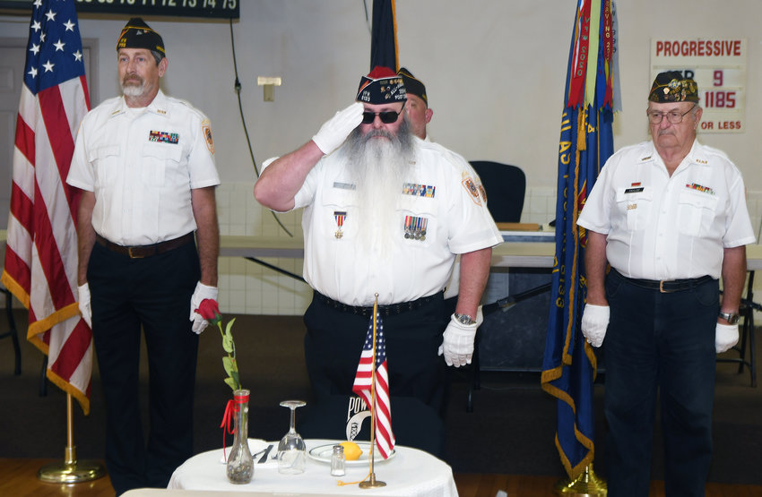 VFW commander Mike Stillman (center) salutes during a missing man ceremony at the beginning of a carry-in dinner. Standing at attention are John Columbo, left, and John Tayloe.