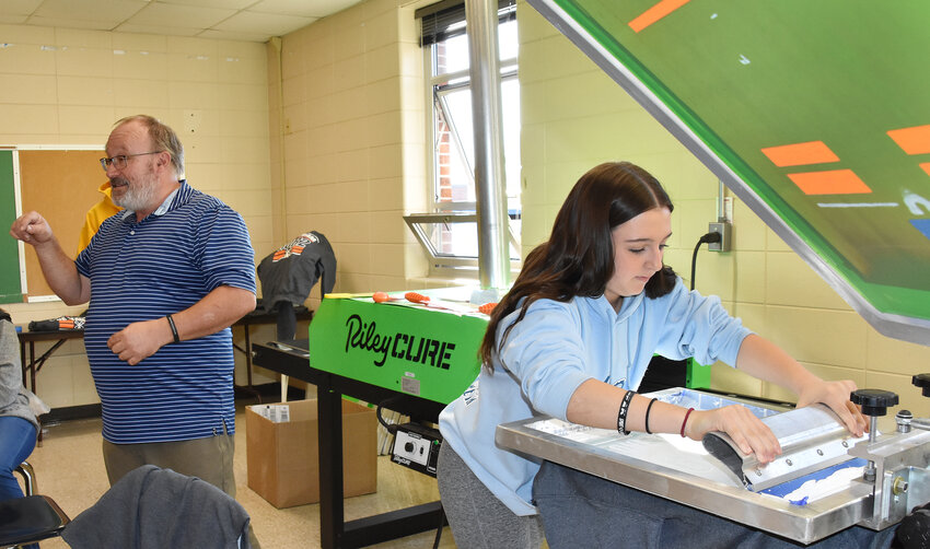 Owensville High School freshman Jenna Hoffman makes a screen printing for a school project Monday during a visit by local elected officials as teacher Rick Hardy explains how the industrial design class creates clothing to sell to benefit the program.