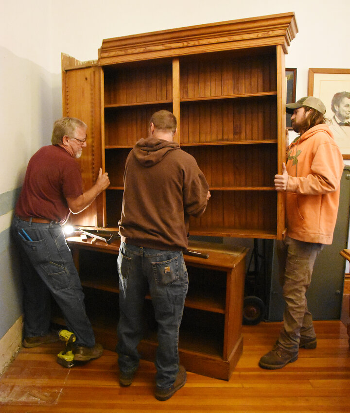 Glen Englert removes a built-in shelving unit from the Gasconade County Courthouse Commission&rsquo;s meeting room with help from B&amp;M Lawn Care staff on Thursday. The unit, believed to have been constructed in the 1930s, was moved to a second-floor office space used by juvenile court staff. Removal was necessary to make room for election equipment which is being relocated from its storage site adjacent to the Commissioner&rsquo;s room to make room for an elevator which is being installed. County Clerk Lesa Lietzow said she regrets losing the storage space but did not want to see plans for an elevator scrapped after waiting 30 years for one to be installed. Her predecessor, the late Roger Prior, had first made the pitch for an elevator when he served as clerk.