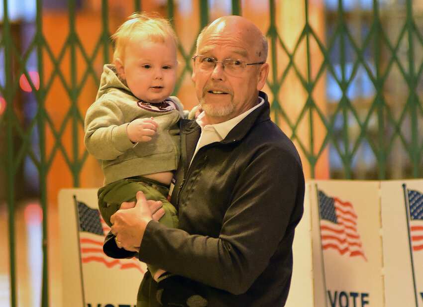 RURAL CANAAN 111th precinct election official Kurt Keller holds 14-month-old Dakota Zelch while the youngster’s father, Noah, was casting his ballot April 2 at Owensville High School.  It was the first election for the boy and his father.